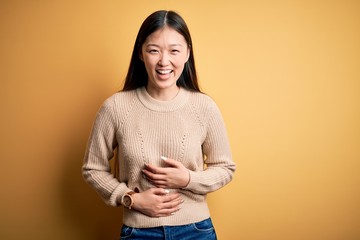 Young beautiful asian woman wearing casual sweater over yellow isolated background smiling and laughing hard out loud because funny crazy joke with hands on body.