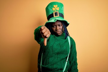 Sticker - Plus size african american woman with braids wearing green hat with clover on st patricks day looking unhappy and angry showing rejection and negative with thumbs down gesture. Bad expression.