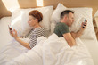 © Space_Cat - Young married couple using their mobile phone in bed ignoring each other as strangers. Relationship and communication problems and internet social network addiction