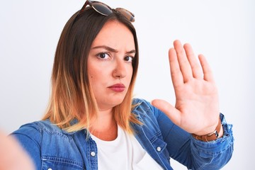 Sticker - Young beautiful woman wearing denim shirt  standing over isolated white background with open hand doing stop sign with serious and confident expression, defense gesture