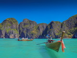 Fototapeta Uliczki - view of long-tail boats floating and running in blue-green sea with rock mountains and blue sky background, Ao Loh Samah Bay, Mu Ko Phi Phi islands, Krabi, southern of Thailand.