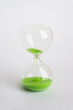 © SergeVo - Hourglass with green sand on white background.
