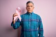 © Krakenimages.com - Middle age handsome grey-haired man holding pink cancer ribbon over isolated background with a confident expression on smart face thinking serious