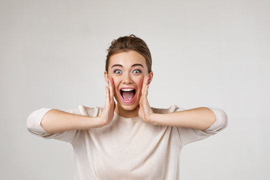 portrait of young surprised beautiful woman screaming with shocked facial expression on gray backgro