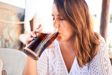 Young beautiful woman sitting at restaurant enjoying summer vacation drinking soda