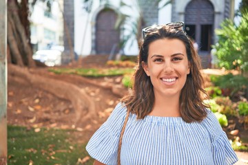 Wall Mural - Young beautiful woman smiling happy walking on city streets by the church on a sunny day of summer