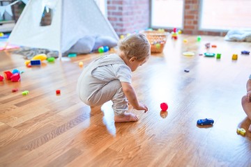 Adorable blonde toddler playing around lots of toys at kindergarten