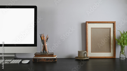 Fotomural Cropped shot of Computer with white blank screen, mouse and keyboard putting on black wooden table next to pencil holder, olden book, coffee cup, picture frame and potted plant
