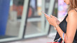 © Prathankarnpap - Close-up woman in black singlet using smartphone while standing with carrying a shopping bags after finished shopping at the urban shopping center with blurred entrance as background.