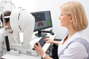 Optometrist woman checks girl eyesight. Diagnosis of eye anterior segment and tomography of boy eyes. Vision correction