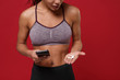 © ViDi Studio - Cropped image of young african american sports fitness woman in sportswear posing working out isolated on red wall background. Sport exercises healthy lifestyle concept. Hold mobile phone, earpods.