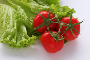 Red fresh tomatoes three pieces and green lettuce leaves lie on a white plain background. Vegetarian diet. Selective focus.