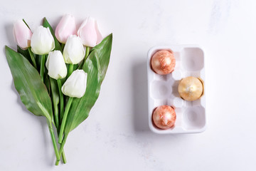 Wall Mural - Golden Easter Eggs in ceramic egg tray with pastel tulips on stone marble background. Easter background or easter concept.