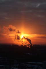 Wall Mural - red sun at sunset or dawn at dusk low above the horizon shrouded in smoke from the chimneys of the p