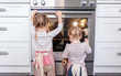 © Cavan Images - Toddlers looking into oven at baking cookies