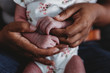 © Cavan Images - Ethnic female hands holding tiny waxy hands of multiracial newborn