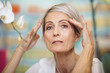 © Cavan Images - Portrait of 67 year old woman holding her hands near eyebrows