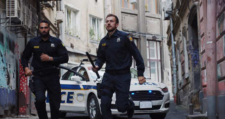 Police patrol car arrives at crime scene. Bottom view professional cops with handguns running in the street performing duties in the city.