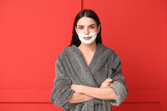 Young woman with shaving foam on her face against color background. Concept of feminism