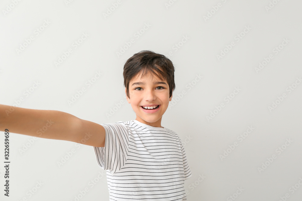 Cute little boy taking selfie on light background