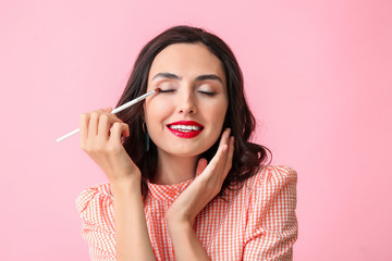 Wall Mural - Beautiful young woman applying makeup on color background