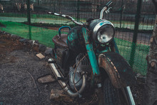 Old Rusty Motorcycle Near Fence On Ground. Close Up Of Abandoned Broken Motorbike.