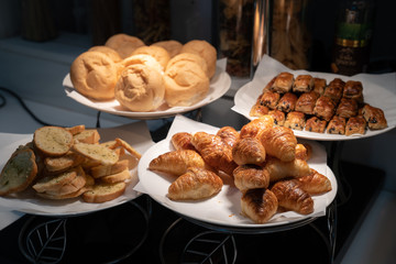 Croissant and bread on paper and white dish in the dark are decorated in tungsten light from lamp.