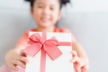 Wall Mural - Little asian girl smile and excited and holding red gift box on sofa in living room background.child holding gift box in Christmas and New year concept.