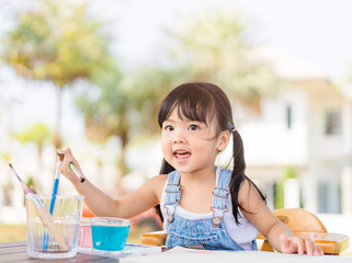 Adorable little asian girl holding a paintbrush and working on a painting watercolor for art class in school.Confidence Positivity Freedom Be Creative Concept.