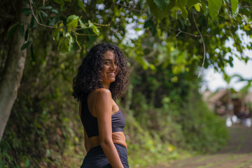 natural lifestyle portrait of young attractive and happy hipster woman with curly hair in fitness clothes enjoying nature outdoors smiling cheerful exploring rural road