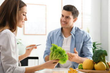 Poster - Young nutritionist consulting patient at table in clinic