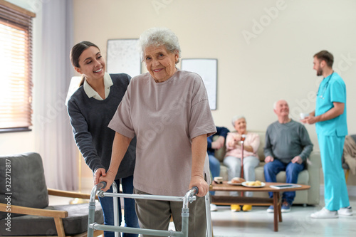 Fototapeta na szkło Opieka pracownik pomaga starszej kobiecie z piechurem w hospicjum geriatrycznym