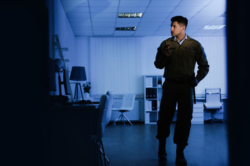 Professional security guard with portable radio set in dark office