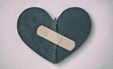 two parts of red broken wooden heart taped by a patch. concept of the forgiveness, renewal of relati