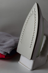 Close-up of an electric steam iron next to a stack of clothes. Modern iron on the table. Everyday homework. Selective focus. Eye level shooting. Vertically