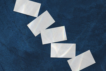 Poster - Close up of empty white rectangle business card mockups with overlay of water shadow and light caustic effect lying diagonally on dark blue concrete background. Flat lay, top view. Open composition.