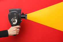 Female Hand Holding Old Style Film Movie Camera Imitating Shooting Process On A Red Background