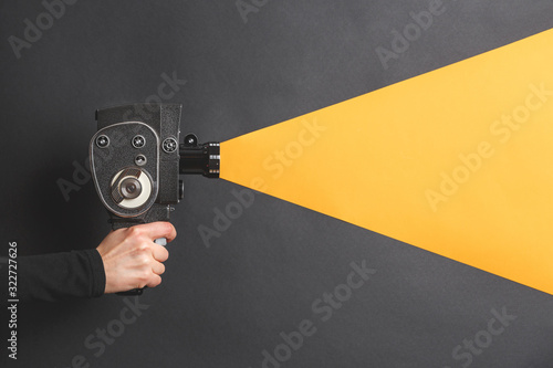 Fototapeta Female hand holding old style film movie camera imitating shooting process on a black background