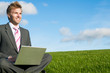 © PeskyMonkey - Smiling businessman sitting outdoors in a sunny green meadow working on his laptop computer