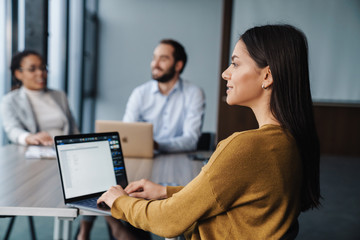 Wall Mural - Image of young female and male colleagues working on laptops in office