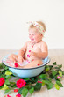 Little cute baby girl is sitting in a basin with pink petals and strawberries.