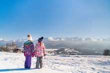 Back View Of Children Standing On Rural Roadway In Snow Looking At Mountain Range In Sunshine