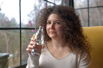 Young woman with curly hair is sitting in a cafe and drinking water