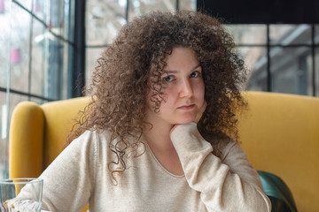 Young woman with curly hair looks thoughtful in a cafe