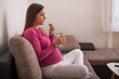 © inesbazdar - Sad pregnant woman drinking pill while sitting on sofa at her home.