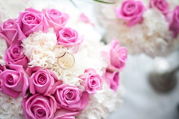 Wall Mural - Bride wedding bouquet. Golden rings on top of pink roses background. Ceremony jewelry symbol of love.