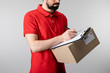 © LIGHTFIELD STUDIOS - Cropped view of delivery man writing on clipboard and holding cardboard box isolated on grey