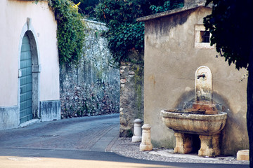 Old medieval italian town street with ancient basin on the corner of the house