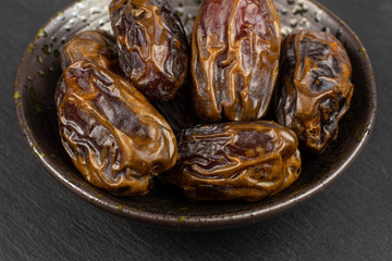 Wall Mural - Lot of whole dry brown date fruit in dark ceramic bowl on grey stone