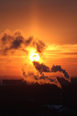 Wall Mural - red sun at sunset or dawn at dusk low above the horizon shrouded in smoke from the chimneys of the p